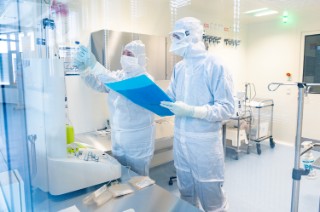 The clinical investigational medicinal products for the LION-1 study are manufactured in the clean room at the Fraunhofer IZI in Leipzig under GMP standards. Two people in protective suits work in the cleanroom.
