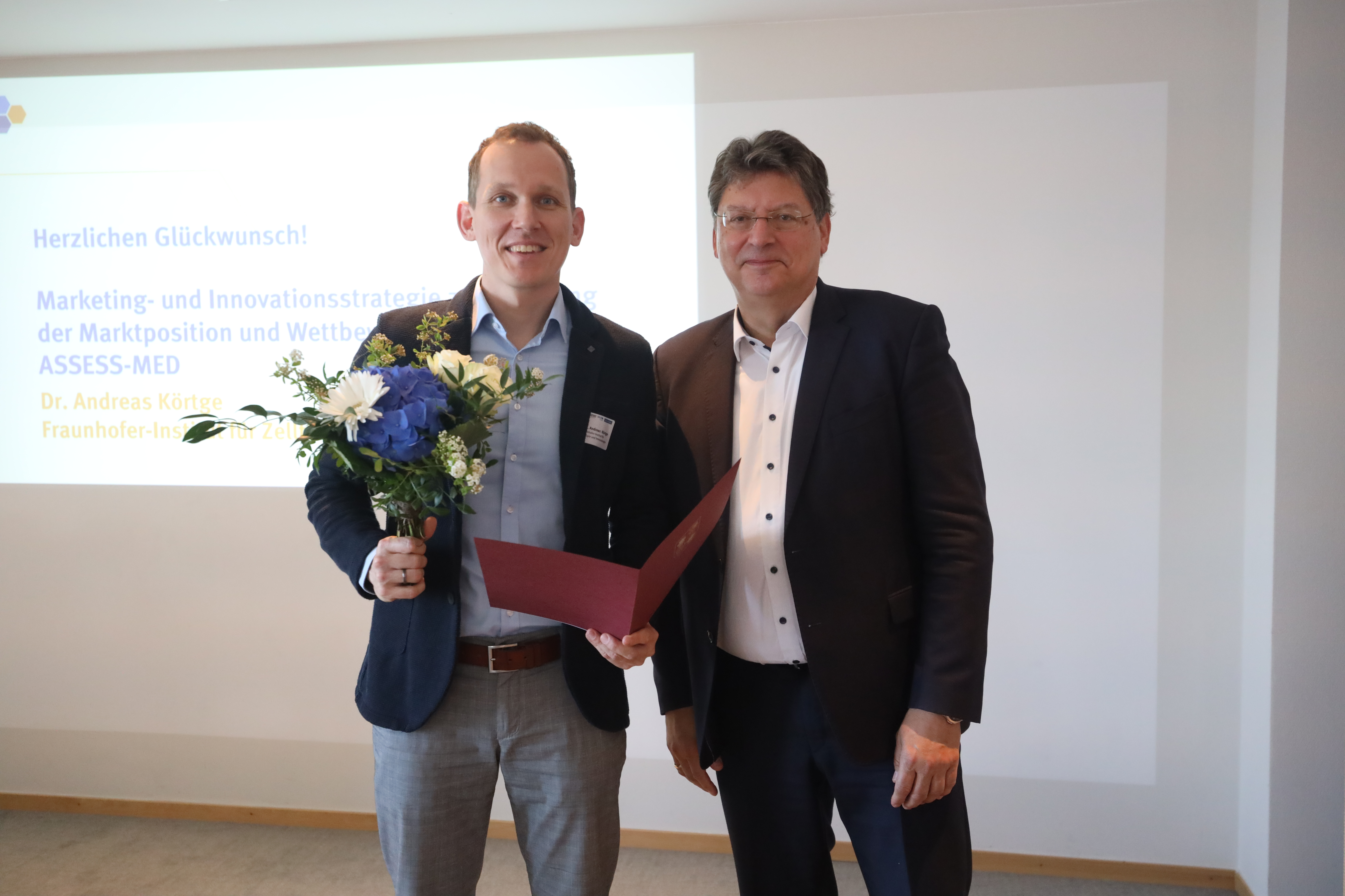 Dr. Andreas Körtge (left) from Fraunhofer IZI received the award from Reinhard Meyer, Minister of Economics of Mecklenburg-Vorpommern. Standing next to scientist Andreas Körtge with a bouquet of flowers and certificate is Reinhard Meyer, Minister of Economic Affairs of Mecklenburg-Vorpommern.
